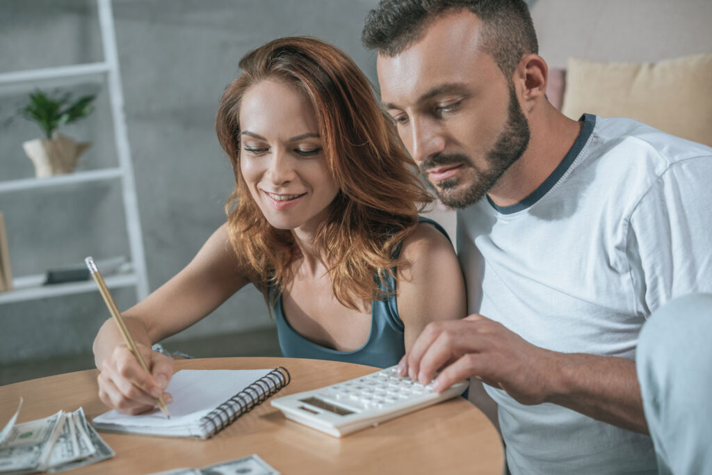 happy couple making a budget with calculator at kitchen table