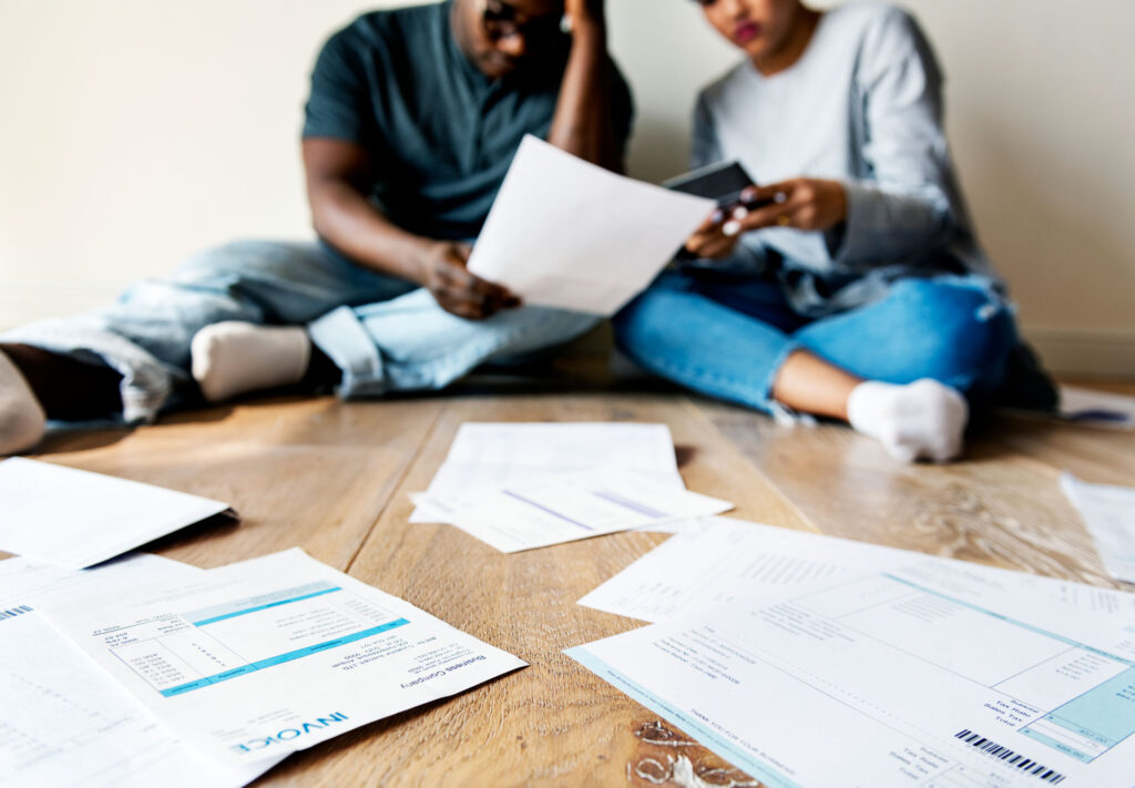 married couple sitting on floor dealing with piles of bills and debt paperwork