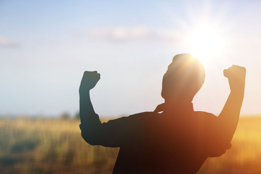 silhouette of man in a field raising his arms in joy