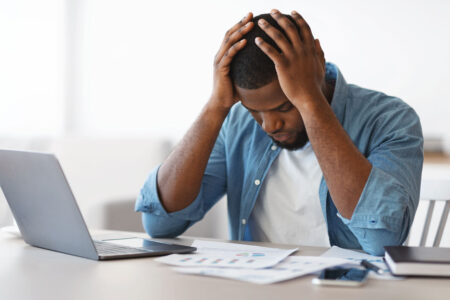 black man at desk with laptop frustrated with bills