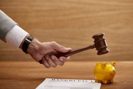 Man holding gavel over piggy bank and bankruptcy form