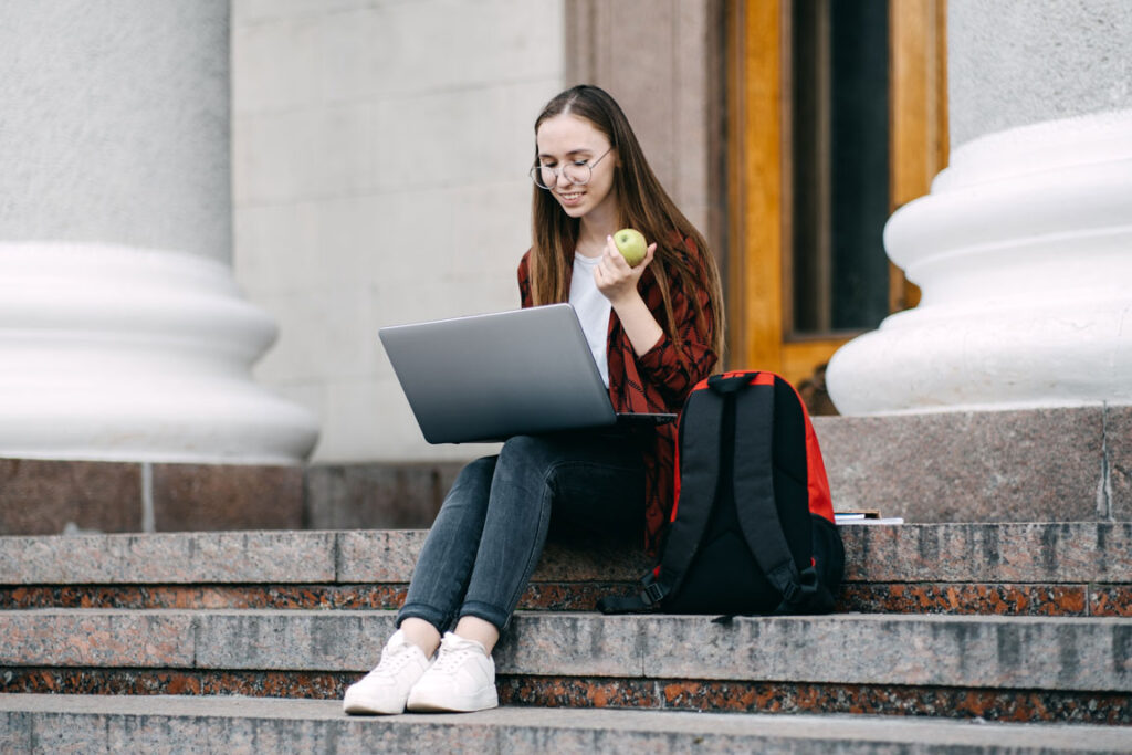 female student sitting on steps with laptop and apple