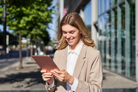 businesswoman smiling outside of office building with a smart tablet